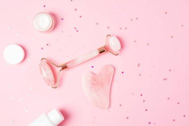 Pembe arka planda kalp şeklinde pırıltıları olan paten ve gua sha masaj kazıyıcısı ve güzellik ürünü. Nemlendirici ve cilt bakım aletleri. Sağlık konsepti. Boşluğu kopyala