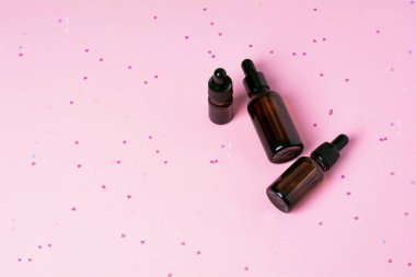 Pembe arka planda, kalp şeklinde pırıltıları olan serum cam şişe. Sıvı deri ya da saç bakım ürünü. Doğal kozmetik konsepti. Ön görünüm, boşluğu kopyala