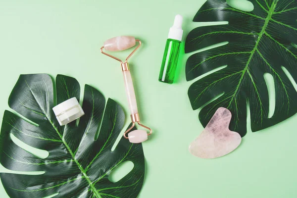 Rodillo y gua sha rascador de masaje y producto comético sobre un fondo verde —  Fotos de Stock