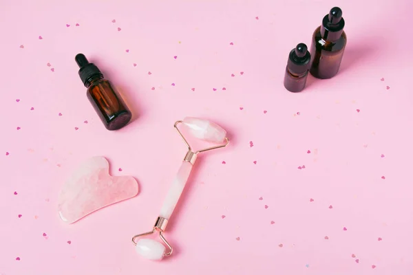 Rodillo y gua sha masaje rascador y productos cométicos sobre un fondo rosa —  Fotos de Stock