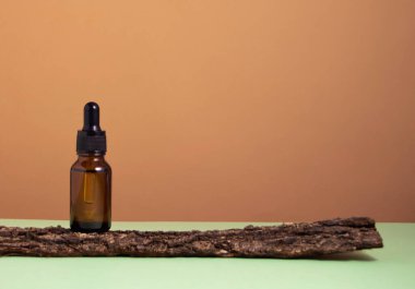 Ağacın kabuğunda serum camı şişesi. Bej ve yeşil arka plan. Sıvı deri ya da saç bakım ürünü. Doğal kozmetik konsepti. Ön görünüm, boşluğu kopyala.