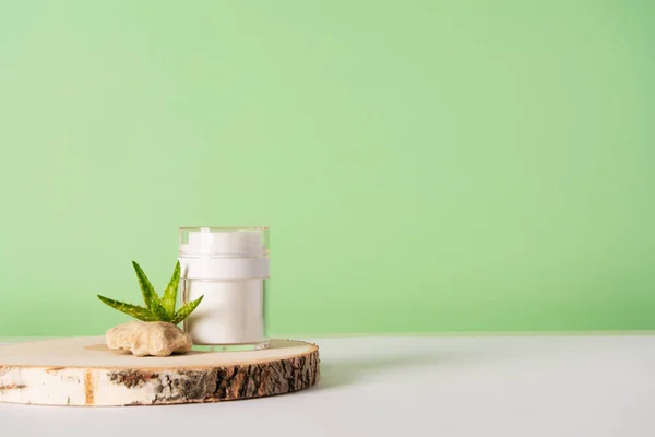 Cosmetic container with cream or other cosmetic product on a wooden podium, stone and aloe. Natural organic cosmetics, healthy beauty concept. Wabi-sabi trend. Foreground.