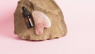 Yakın çekim serumu ya da şişedeki özü ve doğal bir taşın üzerindeki gua sha masaj kazıyıcısı. Bencillik, güzellik ve sağlık konsepti. Metin için boşluk