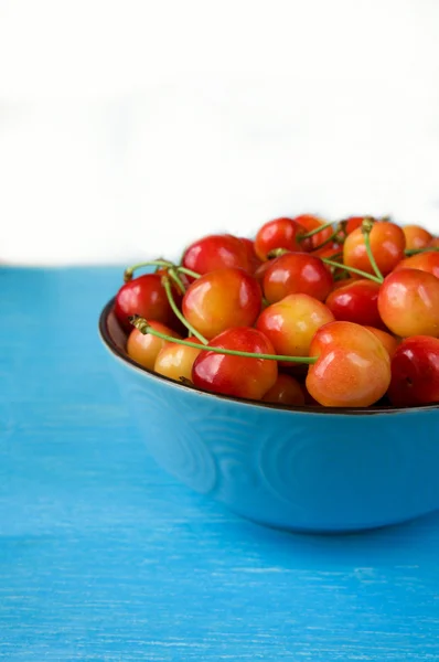 Cereza. Cereza amarilla y roja en un bol sobre un fondo azul — Foto de Stock