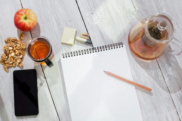 Paper notebook, pencil, cup of tea, apple, cellphone and walnuts on wooden table — Stock Photo, Image