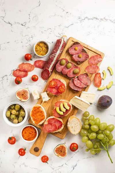 Assortiment de saucisses et fromage, camembert salami brie, raisins, tranches de baguette, olives, sur fond blanc. — Photo