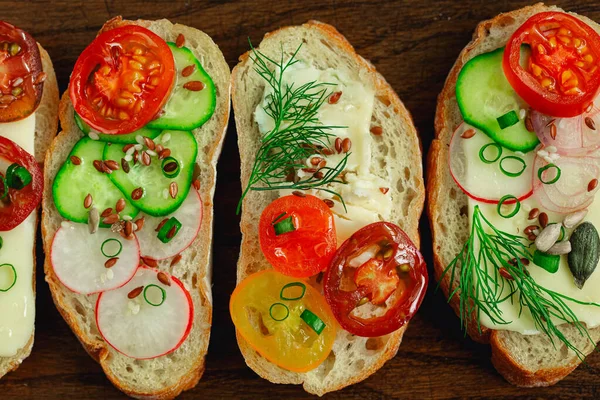 Vollkornbrot oder Sandwiches mit Käse, Gurken, Rettich, Tomaten, Zwiebeln, Dill, Sonnenblumenkürbiskernen auf Holzgrund. — Stockfoto