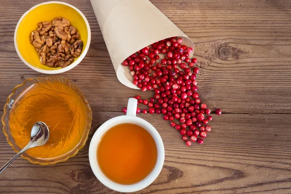 Cowberries, honey, walnuts and a cup of tea on wooden background