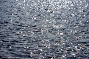 Gün ışığında sakin bir su. Karanlık deniz güneşi yansıtıyor. Dalgalar halinde güneşin yansıması. Sudaki dalgaların dokusu. Güneşli öğle vakti sessiz okyanus. Sakin rüzgar gölet suyunu hareket ettiriyor. 