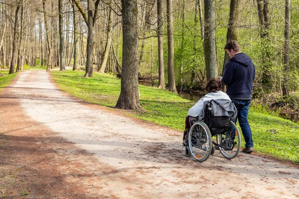 Вид Спины Женщину Инвалидной Коляске Мужчину Идущего Проверяющего Свой Телефон Лицензионные Стоковые Фото