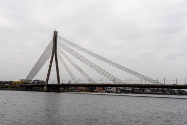 Riga, Daugava nehri üzerindeki kablo köprüsü. Gri sonbahar gününde su, gökyüzü ve köprü depresif gri renkteydi. Ancak nehrin diğer tarafında bazı renkli evler görülebiliyordu..