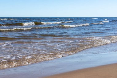 Letonya, Jurmala 'daki Ragakapa Sahili' ne ulaşan dalgalar. Kıyı şeridi sarı kumlu kıyı şeridi güneşli bir günde mavi Baltık deniz dalgalarının kıyıya ulaştığı yer..
