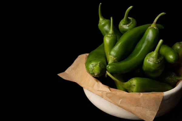 green chili peppers in a bowl with parchment paper on a black background