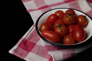 Kırmızı kiraz domatesleri siyah arka planda mutfak havlusuyla bir kasede.