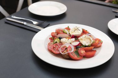 Domatesli İtalyan caprese salatası, mozzarella, fesleğen, kekik, thassos, soğan, turp, kırmızı biber ve beyaz tabakta zeytinyağı..
