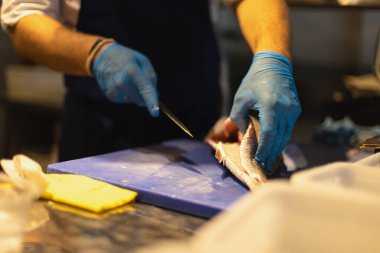 Şef balığı mavi eldivenlerle keser.