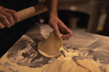 Aşçı hamuru merdaneyle yuvarlıyor. Unlu masa.