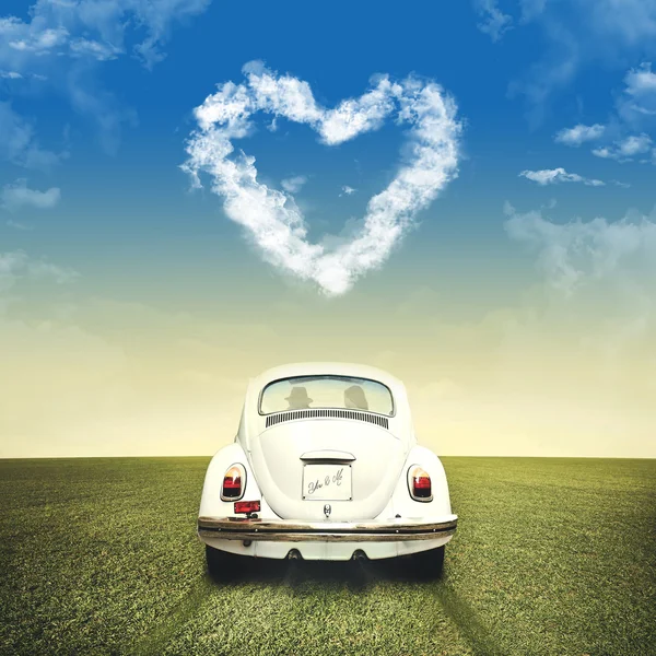 Couple in love driving on a white car under heart shape of clouds — Stock Photo, Image