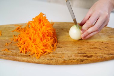 Bıçaklı soğanla dilimlemek ve tahta kesme tahtasının üzerinde rendelenmiş havuçlar..