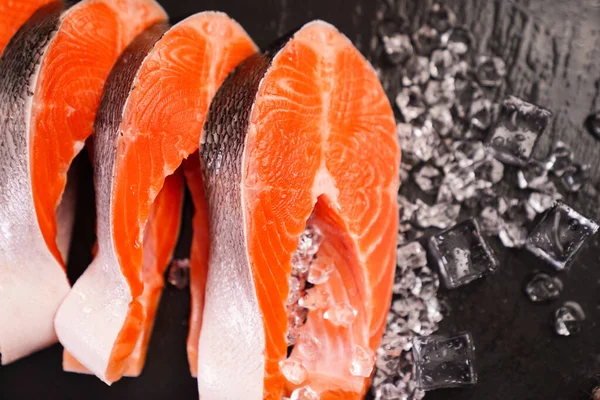Zalm in stukken gesneden op een zwarte stenen plank met ijsblokjes. rode vis. — Stockfoto