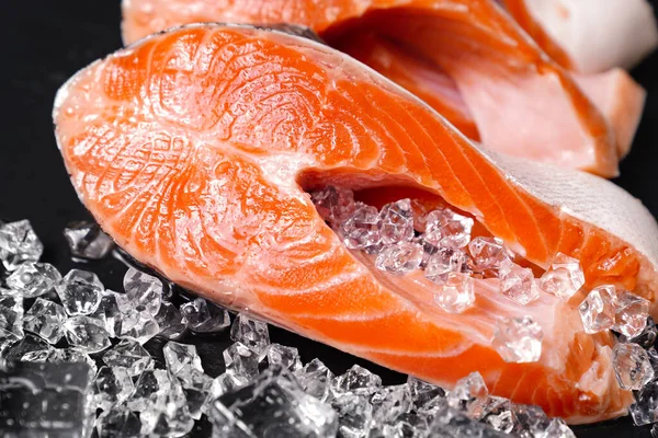 Zalm in stukken gesneden op een zwarte stenen plank met ijsblokjes. rode vis. — Stockfoto