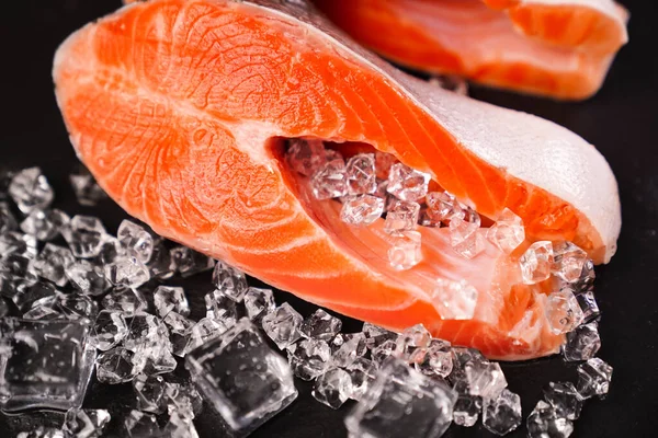 Zalm in stukken gesneden op een zwarte stenen plank met ijsblokjes. rode vis. — Stockfoto