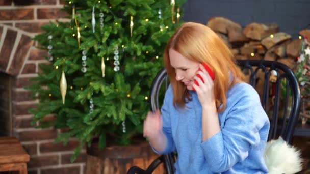 Een vrouw neemt de telefoon op bij de kerstboom. gefeliciteerd aan vrienden. — Stockvideo