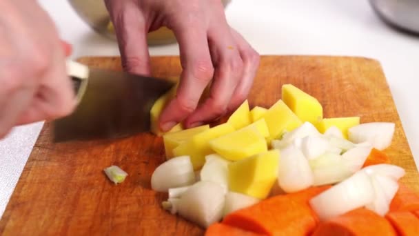 Zanahorias crudas, cebollas y patatas se cortan en cubos grandes en una tabla de cortar. — Vídeos de Stock
