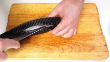 Tuzlanmış füme uskumru, tahta bir kesme tahtasındaki bıçakla parçalara ayrılır.