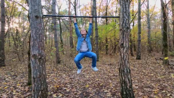 Girl tries to pull up, swings and jumps down off the horizontal bar in the woods — 图库视频影像