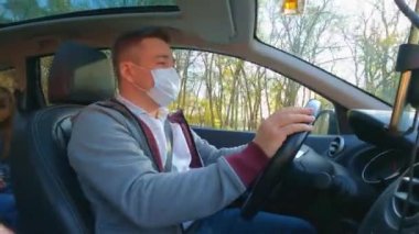Gri ceketli bir adam arabanın direksiyonunda koruyucu bir maske takıyor.. 