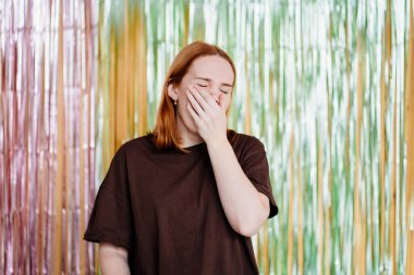 Kahverengi tişörtlü bir kadın, ışıl ışıl bir süslemenin arka planına yaslanır..