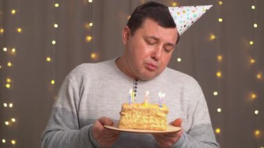 Doğum günü pastası şapkalı üzgün adam mumları söndürüyor. Yaşlanmaktan dolayı üzüntü.