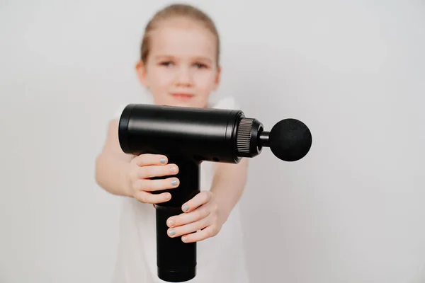 Niña sostiene una pistola de masaje. dispositivo médico-deportivo. —  Fotos de Stock