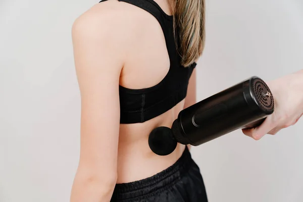 Η έφηβη χρησιμοποιεί όπλο για μασάζ. ιατροαθλητική συσκευή. — Φωτογραφία Αρχείου