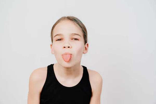 Girl in black T-shirt with collected hair shows tongue on white background. — Stock Photo, Image