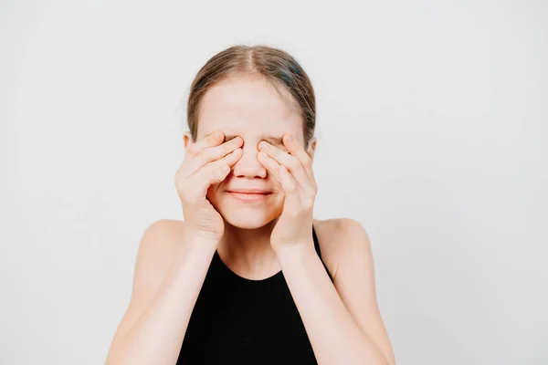 Teenager im schwarzen T-Shirt schließt Augen mit Händen gegen weiße Wand. — Stockfoto