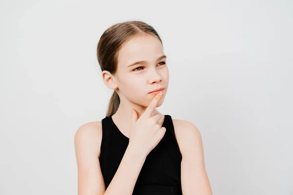 Teen girl with in black T-shirt holds index finger in front of lips and thought. — Stock Photo, Image