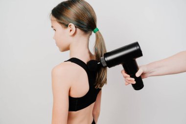 Genç kız masaj silahı kullanıyor. Tıbbi spor aleti eğitimden sonra kas ağrısının azalmasına yardımcı olur, yorgunluğun azalmasına yardımcı olur, vücudun sorunlu bölgelerini etkiler, cildin durumunu iyileştirir.