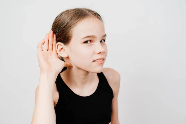 A teenage girl in a black T-shirt holds her hand by her ear and listens. — Stock Photo, Image