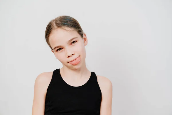 Girl in black T-shirt with collected hair shows tongue on white background. — Stock Photo, Image