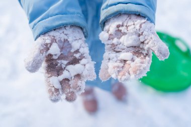 Bir kız kar toplarıyla oynadıktan sonra pembe eldivenlere yapışmış kar gösteriyor..