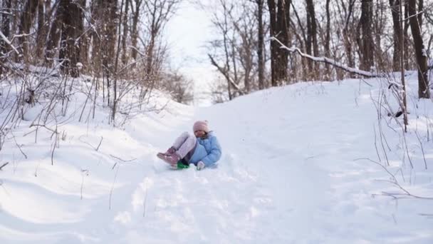 Uma menina adolescente em um casaco azul tenta mover-se em um trenó de um deslizamento de neve — Vídeo de Stock