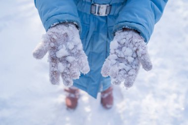Bir kız kar toplarıyla oynadıktan sonra pembe eldivenlere yapışmış kar gösteriyor..