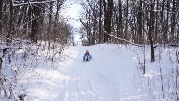 Una adolescente con un abrigo azul trata de moverse en un trineo de un tobogán de nieve — Vídeo de stock