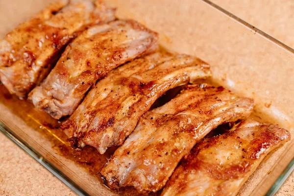 Frito con especias costillas de cerdo en una bandeja para hornear de vidrio sobre un fondo de madera — Foto de Stock