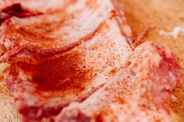 Свиные ребра посыпать солью, черным перцем и паприкой на деревянную доску — стоковое фото