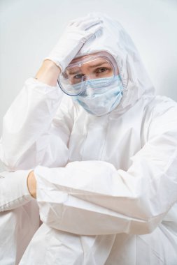 Koruyucu takım elbiseli, gözlüklü, maskeli yorgun bir doktorun portresi.