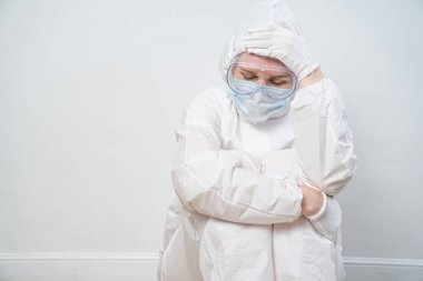 Koruyucu takım elbiseli, gözlüklü, maskeli yorgun bir doktorun portresi.