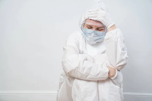 portrait of a tired doctor in protective suit, glasses, mask against white wall